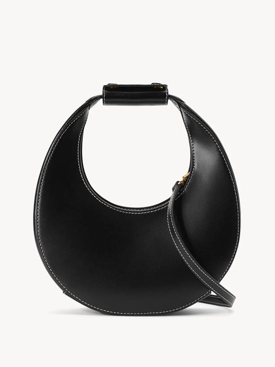 The STAUD Mini Moon Bag in Black features a crescent-shaped leather design with a short stitched handle and thin crossbody strap, shown against a plain white background.