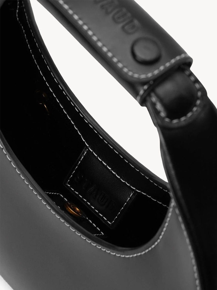 Close-up of the STAUD Mini Moon Bag in Black, featuring smooth leather, visible white stitching, an embossed inner brand label, and a crossbody strap for versatile wear.