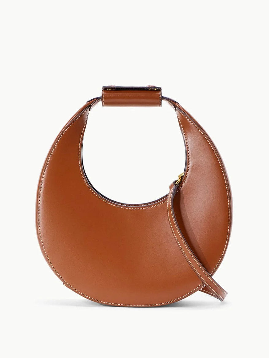 The STAUD Mini Moon Bag in Tan features brown leather with white stitching, a top handle, and a slim crossbody strap, shown against a plain white background.