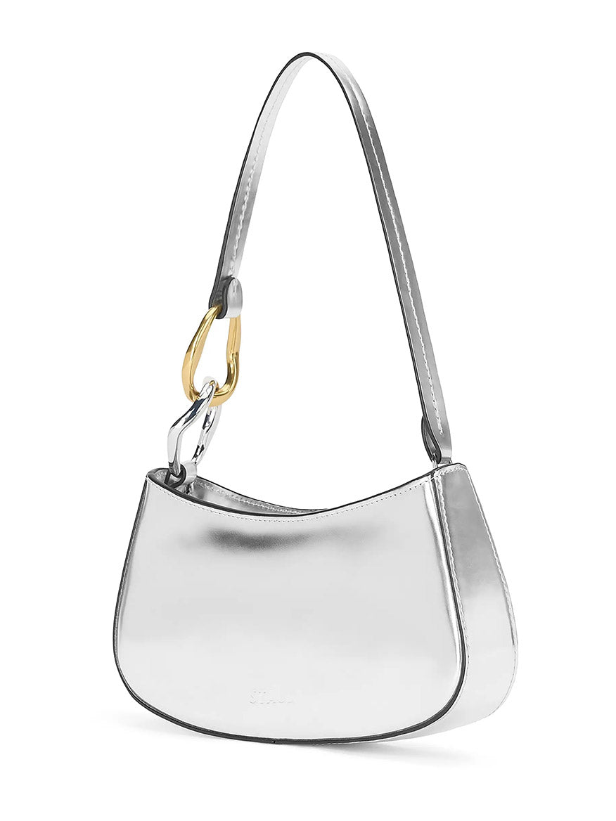 The STAUD Ollie Bag in Chrome is a silver metallic leather shoulder bag with a structured silhouette, single strap, and gold and silver carabiner-style accent on one side.
