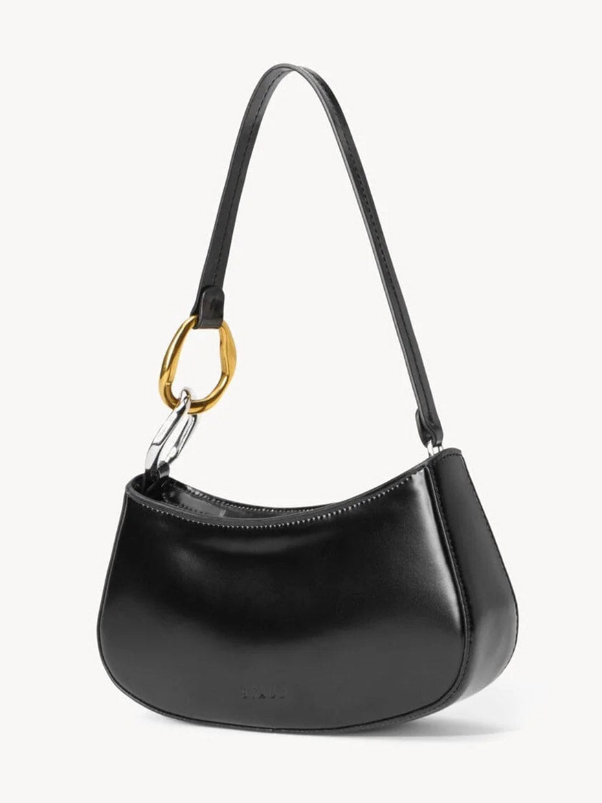 The STAUD Ollie Bag in Black is a polished leather mini shoulder bag with gold oval hardware on one side and a short strap, shown against a plain white background.