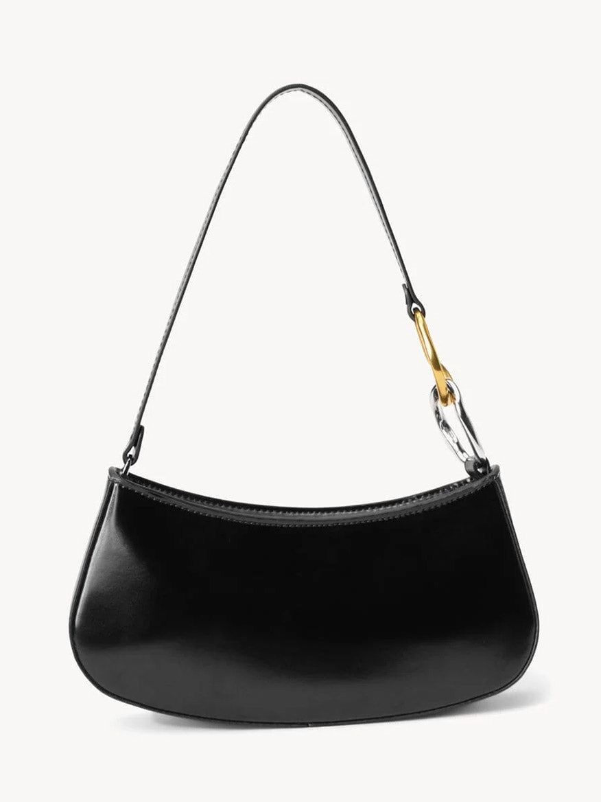 The STAUD Ollie Bag in Black is a polished leather mini shoulder bag featuring a curved bottom, single top handle, and two-tone hardware detail on one side.