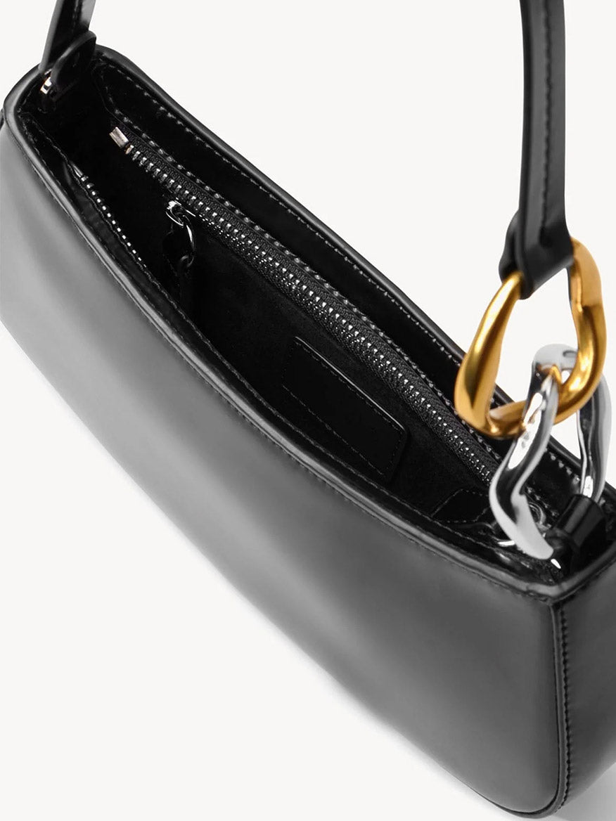 The STAUD Ollie Bag in Black is a polished leather mini shoulder bag with a zippered compartment and a short handle featuring gold and silver two-tone hardware accents.