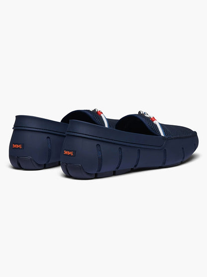 A pair of navy blue Swims Riva loafers against a white background, with red accents on the adjustable back straps.