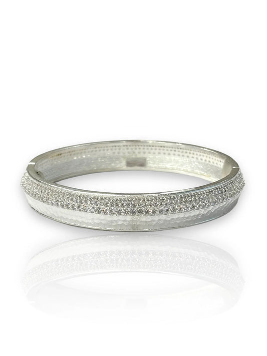 The Tat2 Designs Noma Bangle in Silver Pave features a row of small, clear crystals atop its sterling silver-plated finish, displayed on a white reflective surface.