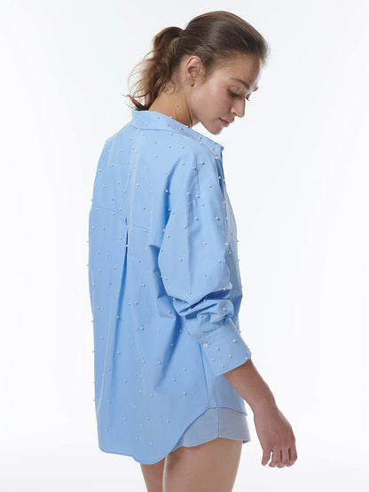 Woman in a THEO The Label Echo Pearly Shirt in Sky Blue with pearl details, viewed from behind.