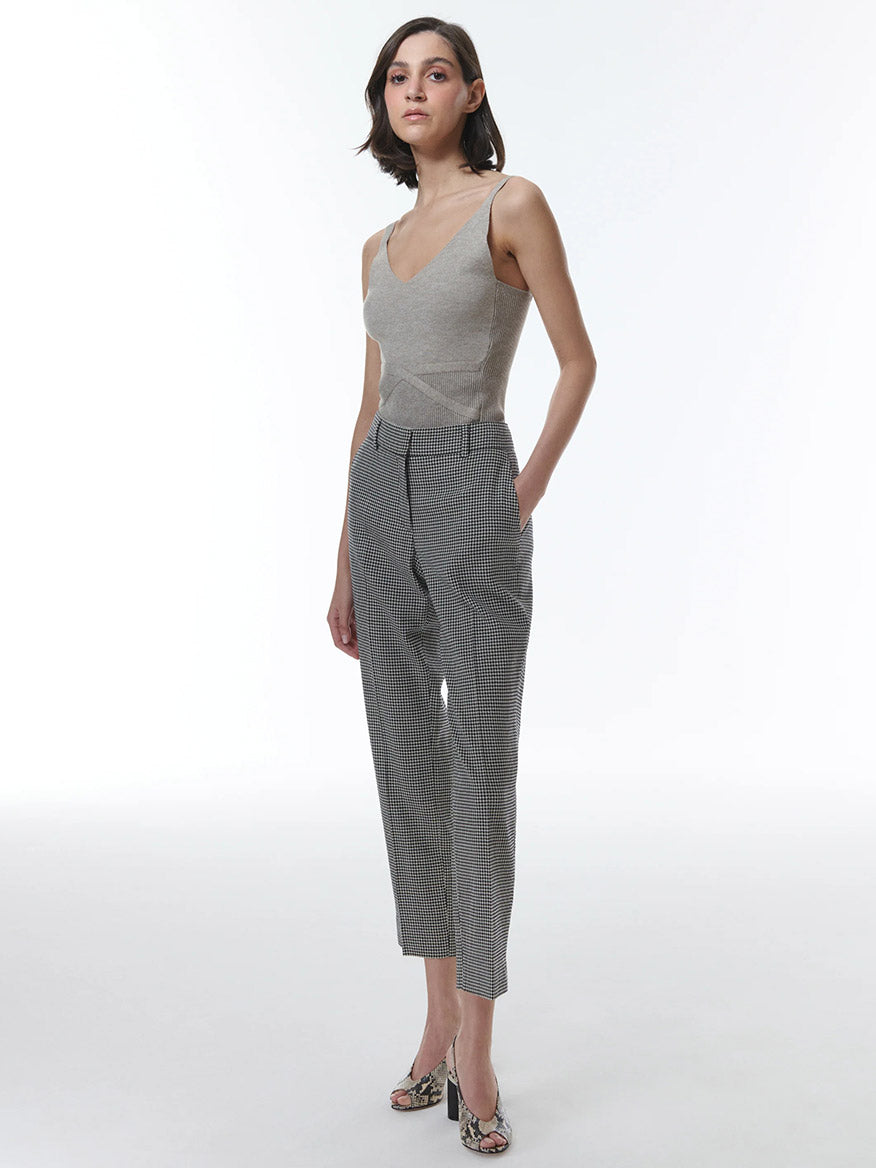 A woman posing in a sleeveless top and THEO The Label Eris Baby Houndstooth Pant in Black/Ivory against a white background.