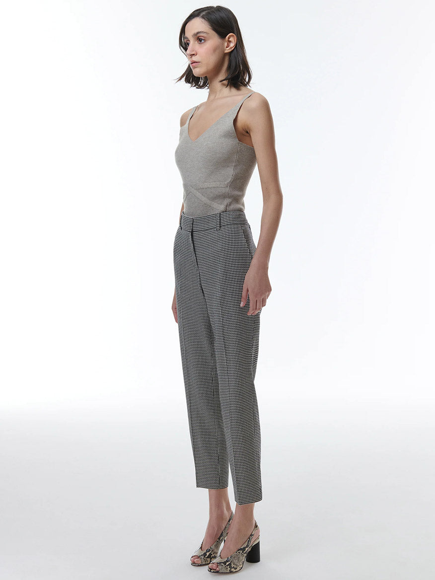 A woman posing in a gray sleeveless top and THEO The Label Eris Baby Houndstooth Pant in Black/Ivory against a white background.