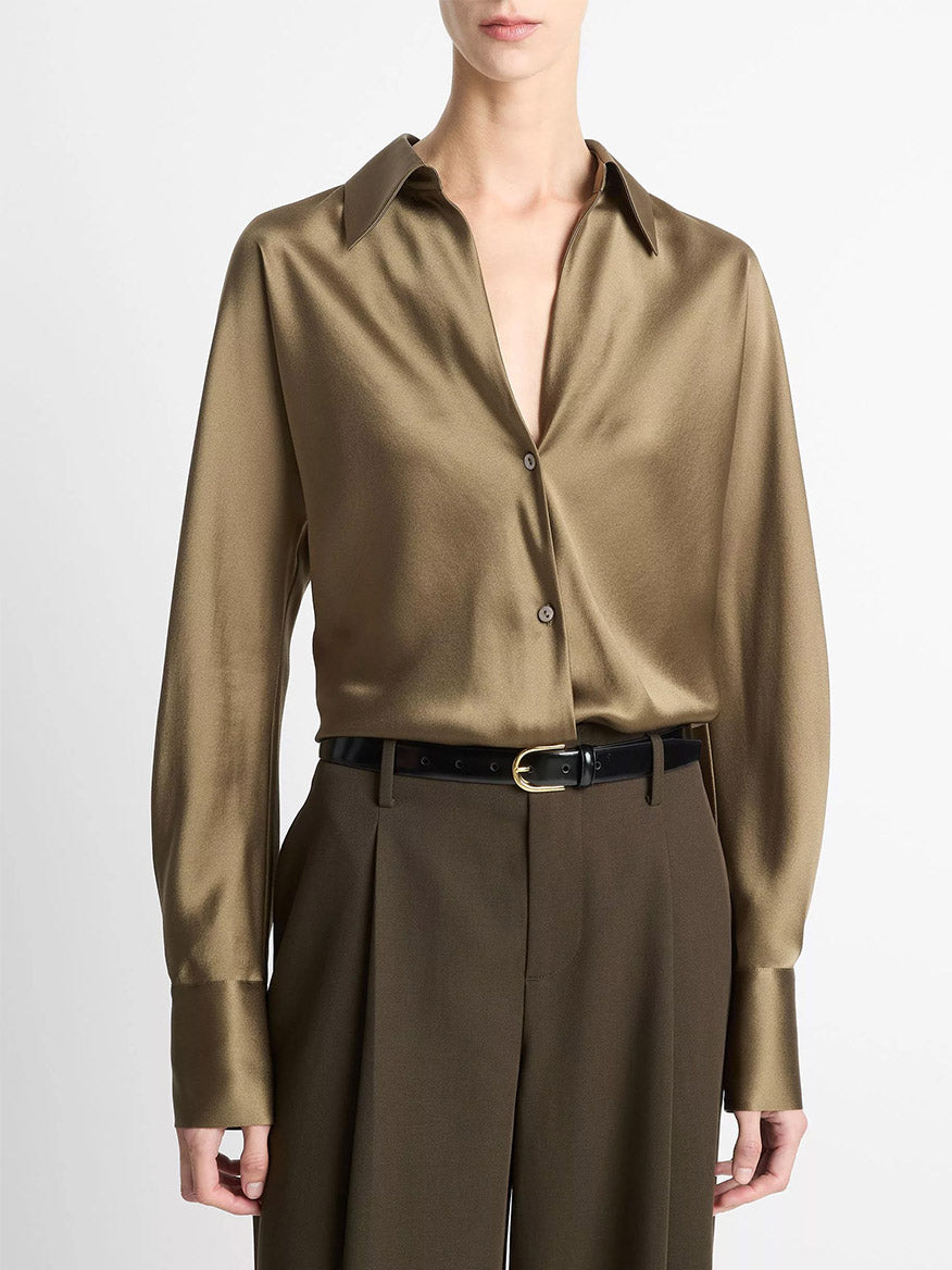 A person wears the Vince Silk Bias Long-Sleeve Blouse in Cypress, tucked into high-waisted, pleated brown trousers with a black belt, standing against a plain background.