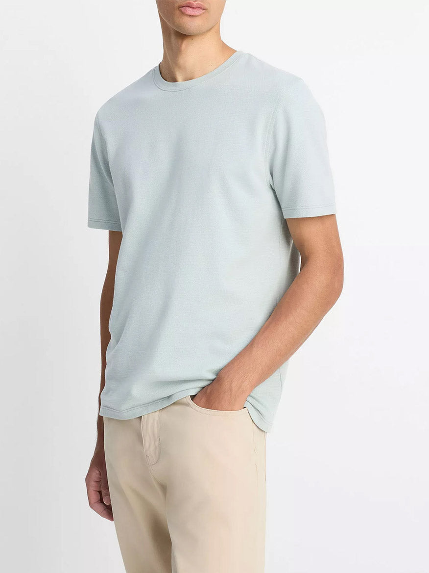 A person wears the Vince Birdseye Jacquard Pima Cotton T-Shirt in Skylight and beige pants, standing against a plain white background with one hand in their pocket.