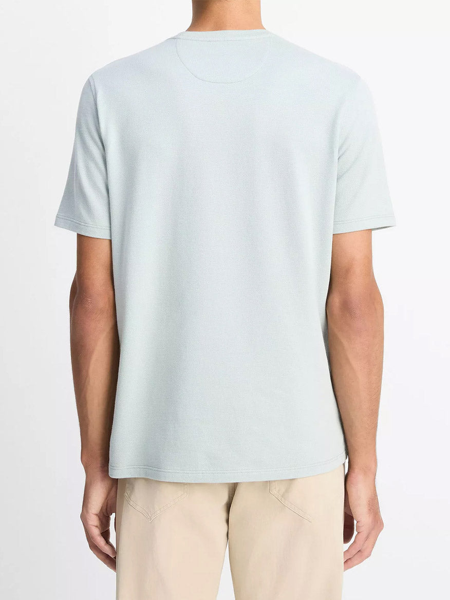 A person stands facing away, wearing the Vince Birdseye Jacquard Pima Cotton T-Shirt in Skylight and beige pants against a plain background.