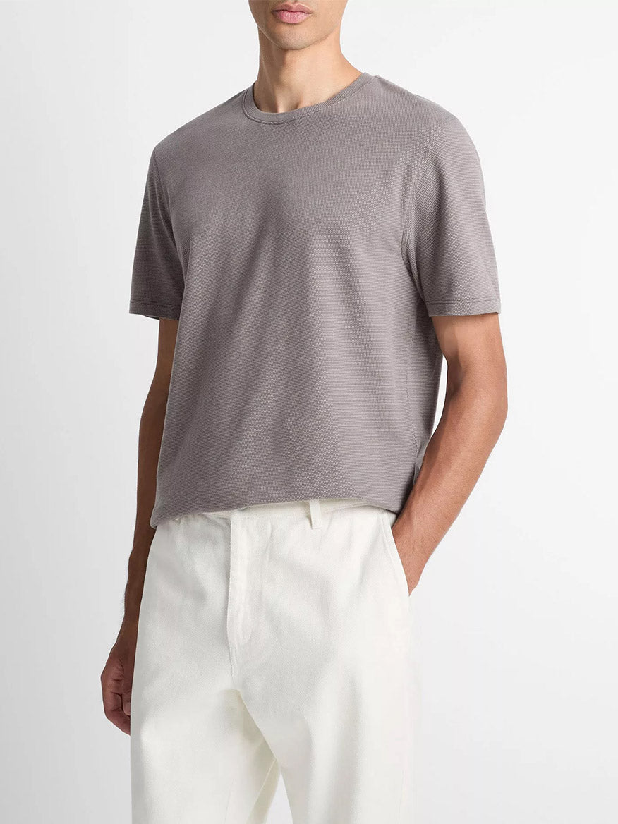A person wearing the Vince Birdseye Jacquard Pima Cotton T-Shirt in Smoke and white pants stands with one hand in their pocket against a plain background.