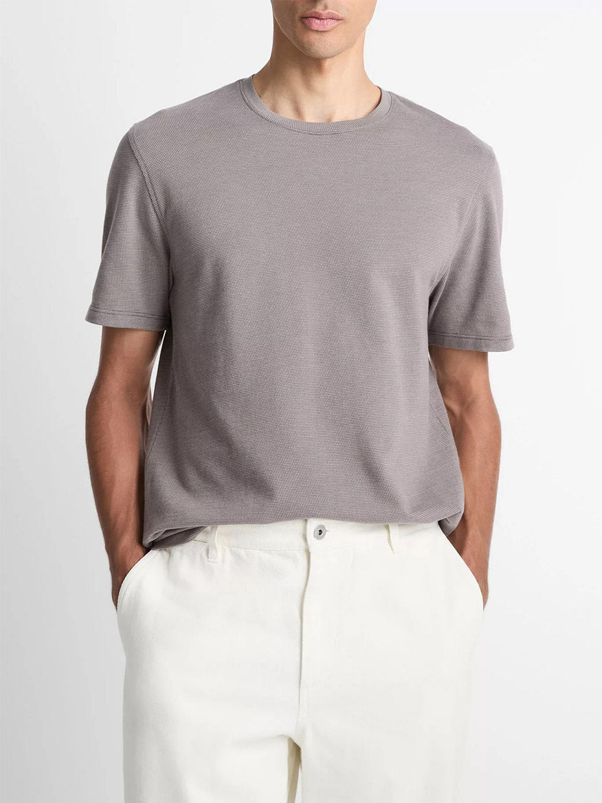 A person wears the Vince Birdseye Jacquard Pima Cotton T-Shirt in Smoke with white pants, standing hands-in-pockets against a plain background.