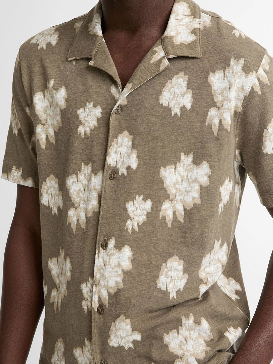 A person wearing the Vince Blurred Roses Short-Sleeve Button-Front Shirt in Kalamata Combo, featuring an abstract beige floral roses motif on a light brown background.