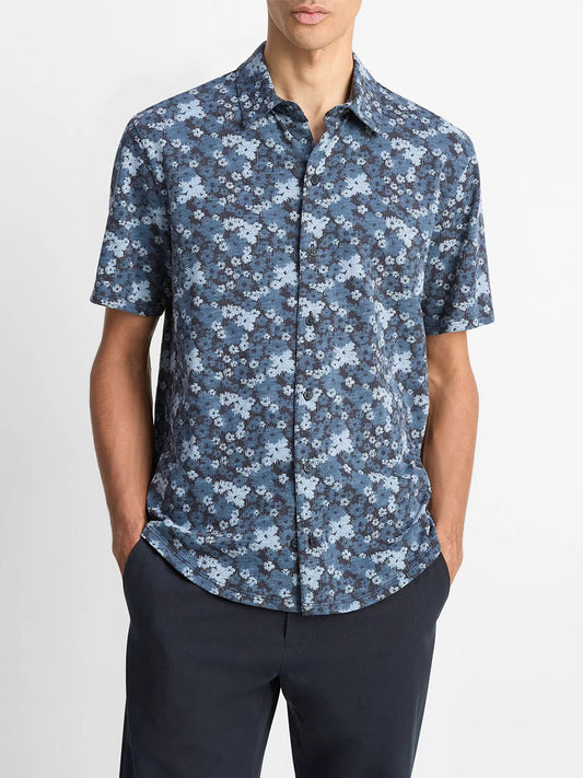 A person models the Vince Floral Slub Cotton Short-Sleeve Button-Front Shirt in Coastal Blue with dark pants, hands in pockets, standing against a plain white background.