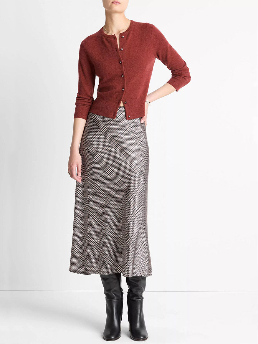 A person wears the Vince Metal-Button Wool & Cashmere-Blend Cardigan in Siena (rust), a grey plaid midi skirt, and black knee-high boots, standing against a plain white background.