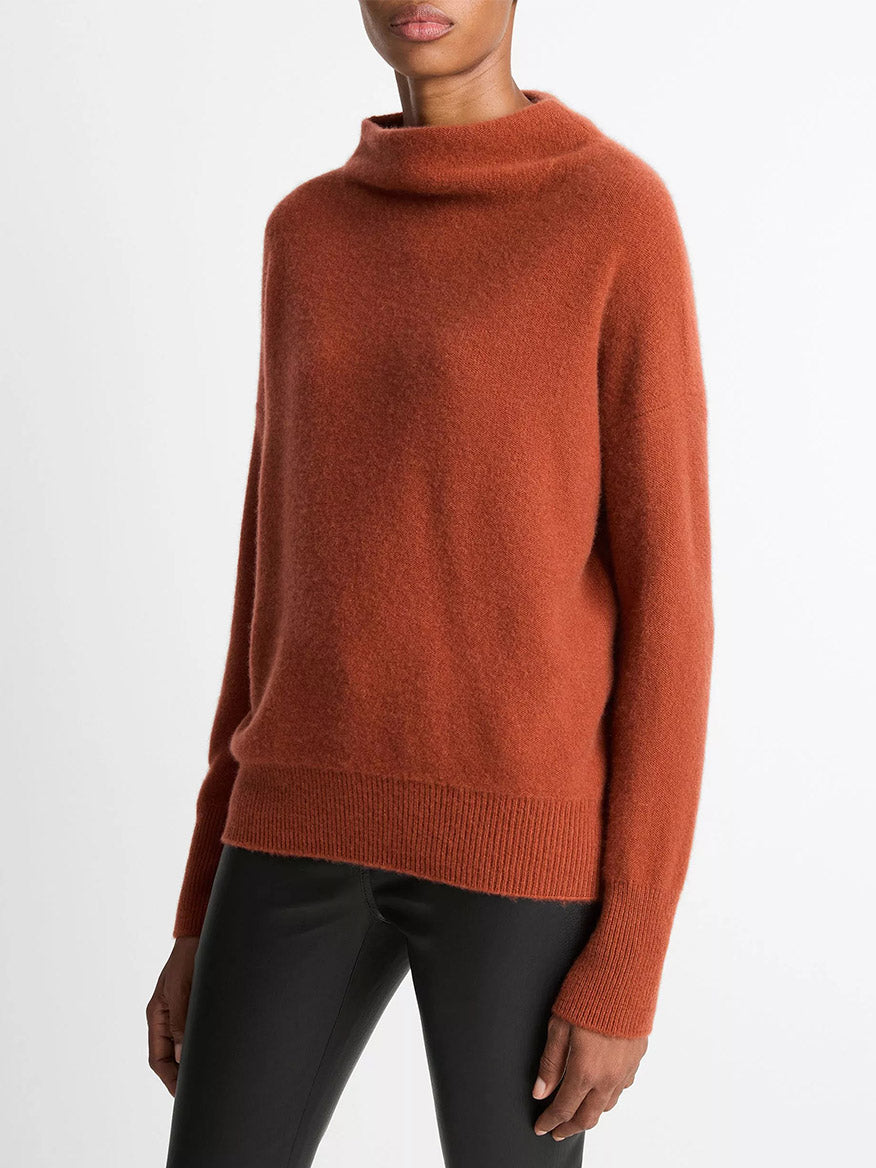 Person wearing a Vince Plush Cashmere Funnel-Neck Sweater in Tuscan Red with black pants, standing against a plain light background.