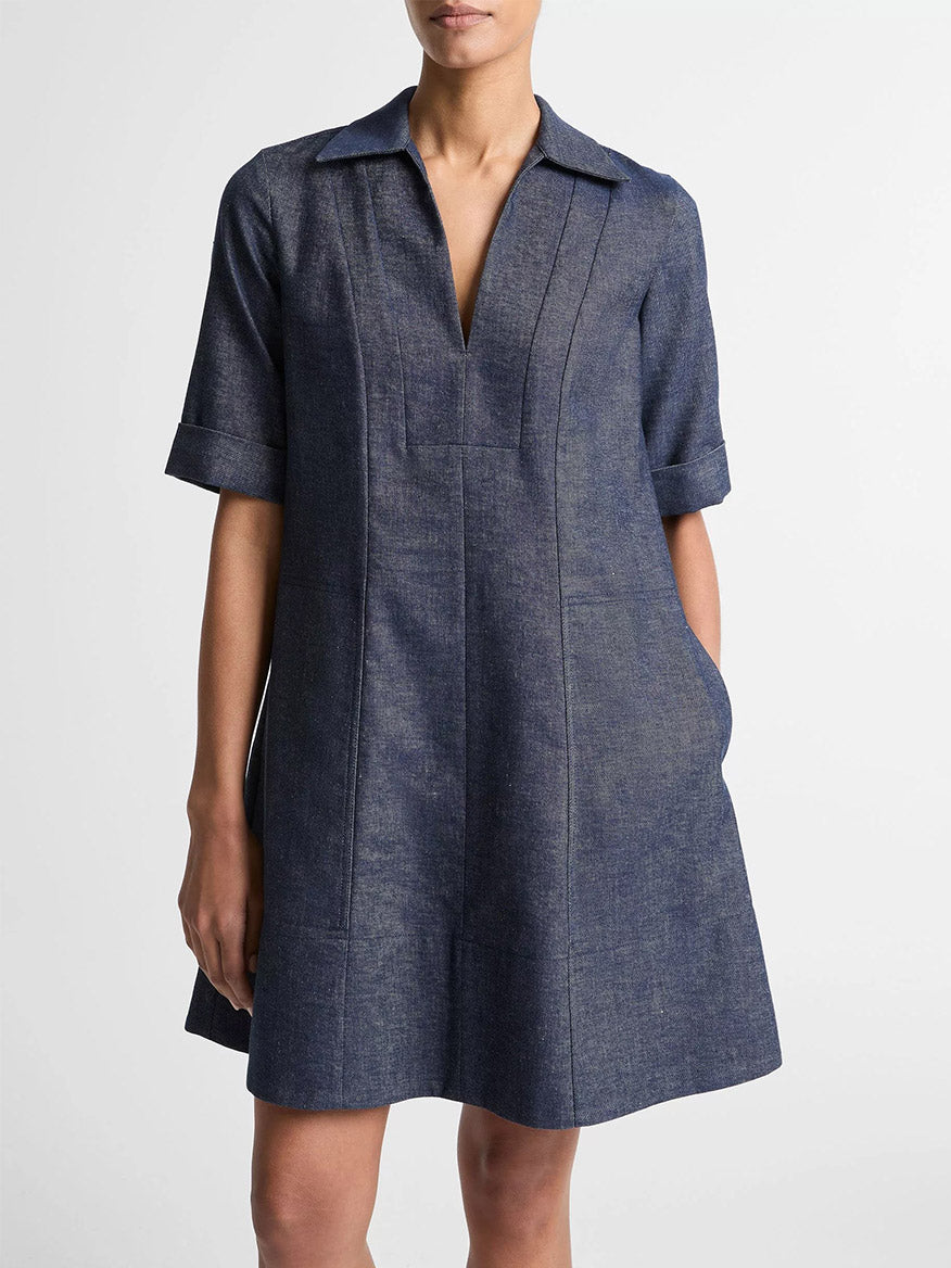 A woman wears the Vince Cotton-Linen Chambray A-Line Dress in Indigo, featuring short sleeves, a collar, and a V-neckline, as she stands against a plain white background.