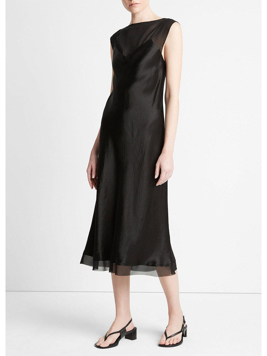 A woman in a Vince Chiffon-Layered Satin Slip Dress in Black with sheer panel details, paired with black heels, standing side-on in a neutral pose.