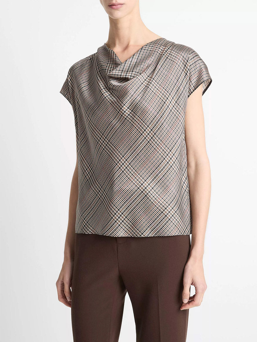 A woman wears the Vince Pressed Plaid Silk Cowl-Neck Blouse in Multi Plaid with brown trousers, standing against a plain white background.