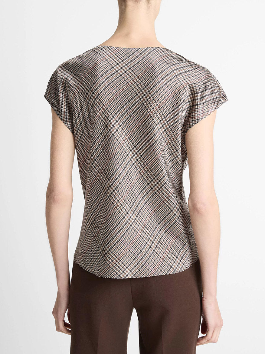 A person faces away, wearing the Vince Pressed Plaid Silk Cowl-Neck Blouse in Multi Plaid with short sleeves, paired with brown pants against a plain background.