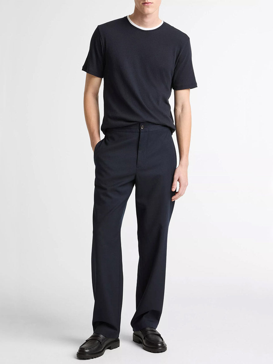 A man stands against a plain background wearing the Vince Cotton Double-Collar T-Shirt in Coastal Blue/Optic White, paired with black trousers and black loafers, his hands in his pockets.