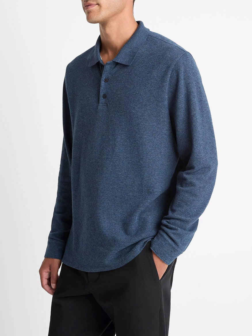 A man wears the Vince Heathered Double-Face Cotton-Blend Polo Shirt in Heather Coastal Blue/Heather Fog with black pants against a plain white background, making it an ideal transitional wardrobe layer.