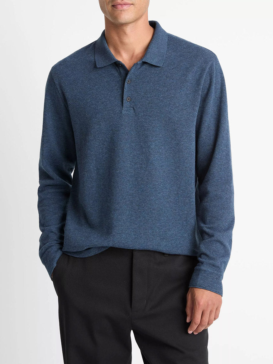 A man wears the Vince Heathered Double-Face Cotton-Blend Polo Shirt in Heather Coastal Blue/Heather Fog with black pants, standing with one hand in his pocket against a plain white background.