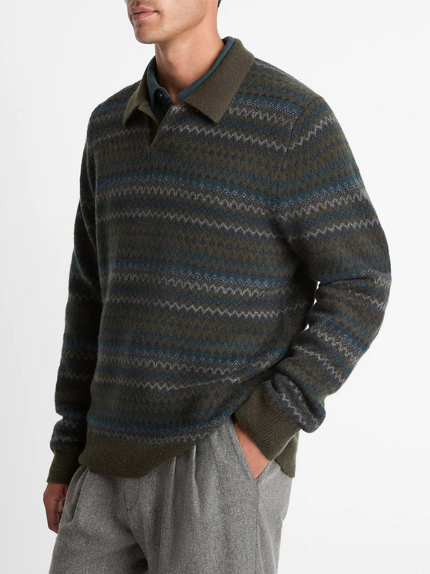 A man wears the Vince Fair Isle Wool-Cashmere Johnny-Collar Sweater in Dark Leaf Combo with gray pants, standing with one hand in his pocket against a plain white background.