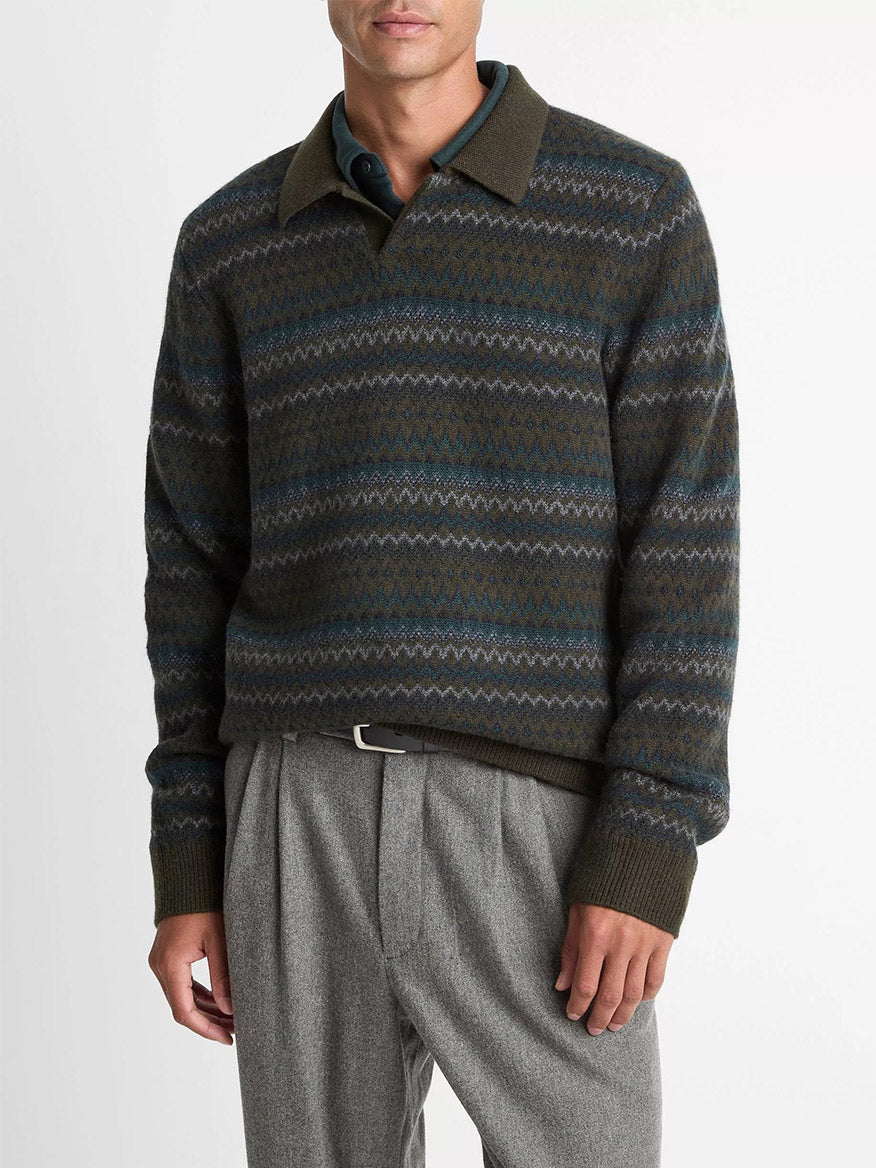 A man wearing the Vince Fair Isle Wool-Cashmere Johnny-Collar Sweater in Dark Leaf Combo, paired with grey trousers and a black belt, stands against a plain white background.