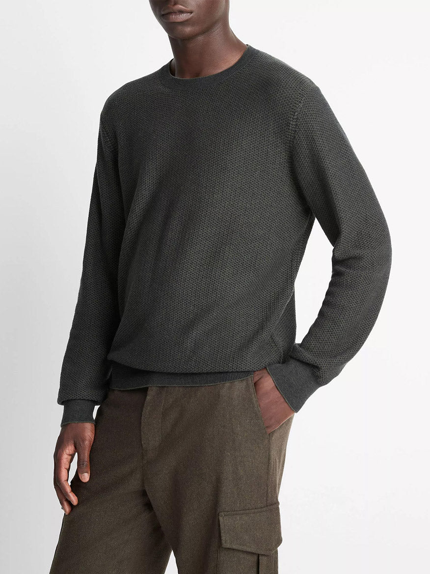 A person stands against a plain white background wearing the Vince Geo-Jacquard Wool-Blend Crew Neck Sweater in Driver Green/Coastal Blue and brown cargo pants.