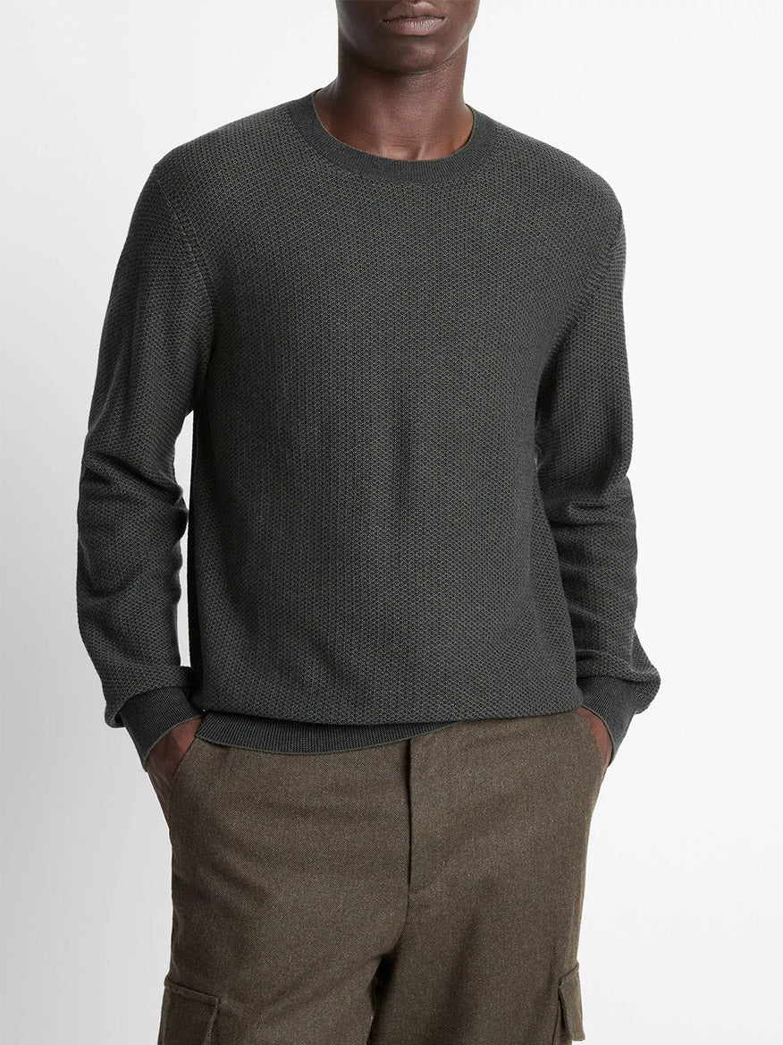 A person wears the Vince Geo-Jacquard Wool-Blend Crew Neck Sweater in Driver Green/Coastal Blue with brown pants, standing hands-in-pockets against a plain background.