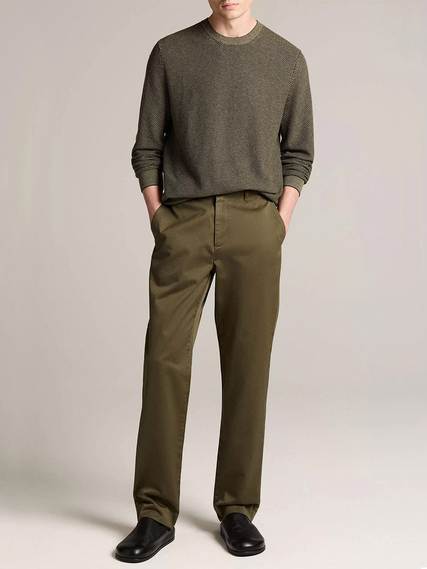A person wearing the Vince Geo-Jacquard Wool-Blend Crew Neck Sweater in Midnight Garden/River Sand, paired with olive-green trousers and black shoes, stands with hands in pockets against a plain background.