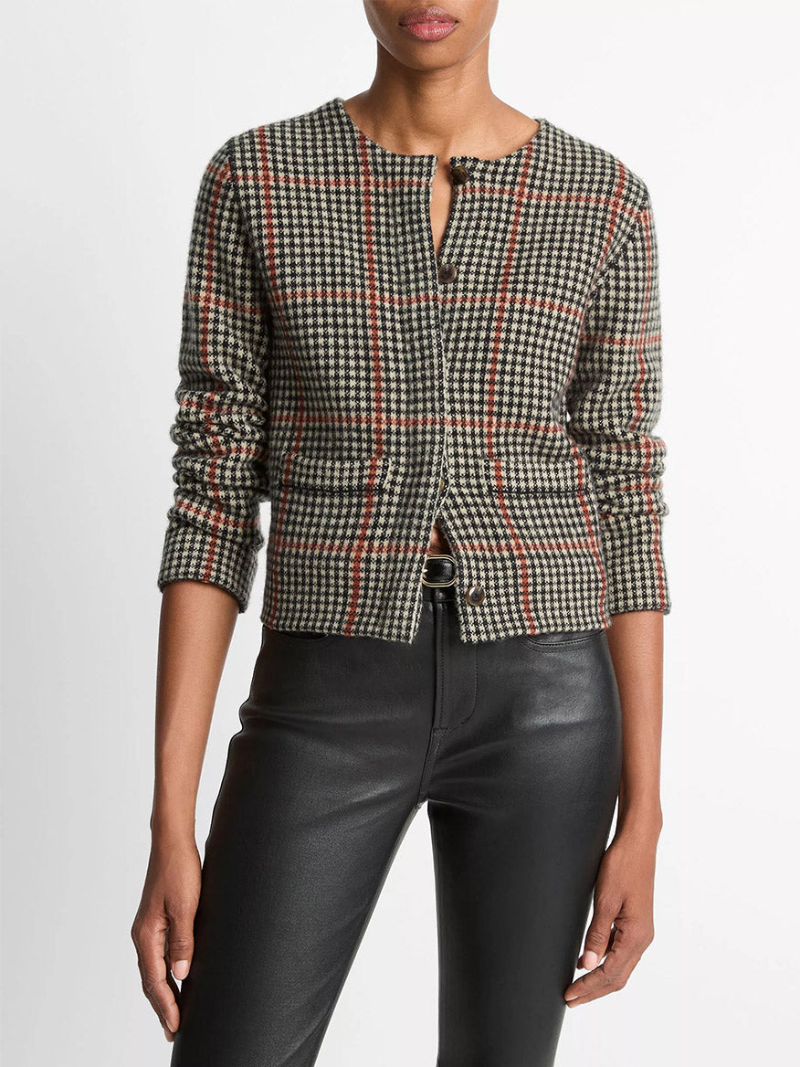 A person wears the Vince Glen Plaid Wool-Cashmere Cardigan Jacket in Cobblestone/Black Combo with black faux leather pants, standing against a plain white background.