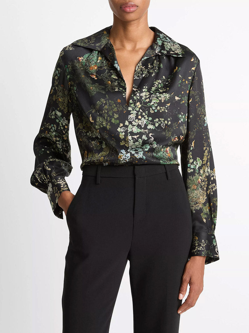 Someone wears the Vince Smocked Grape Vine Silk Long-Sleeve Blouse in Black Sky, featuring a deep collar and smocked ruching, paired with high-waisted black trousers.