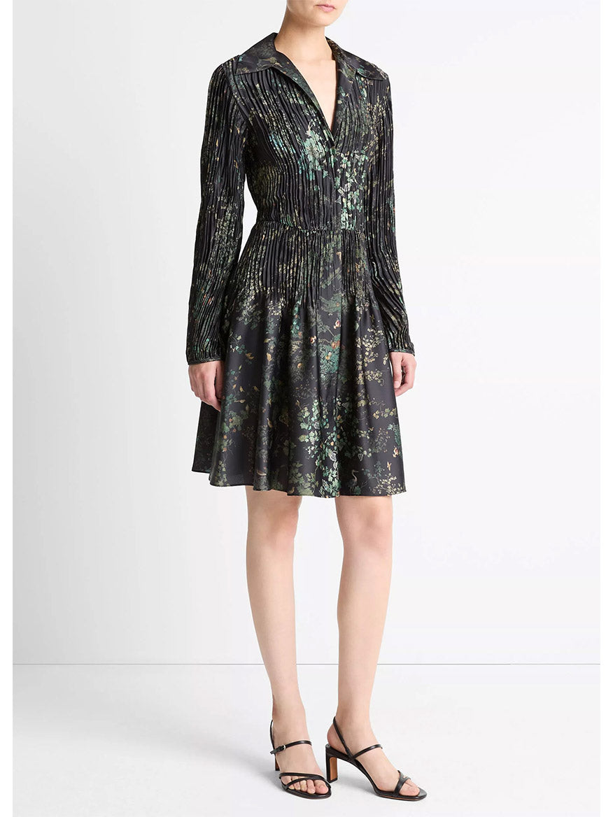 A woman wears the Vince Grape Vine Crushed Satin Shirt Dress in Black Sky, featuring long sleeves and an elasticized waist, paired with black strappy heeled sandals, standing against a plain white background.