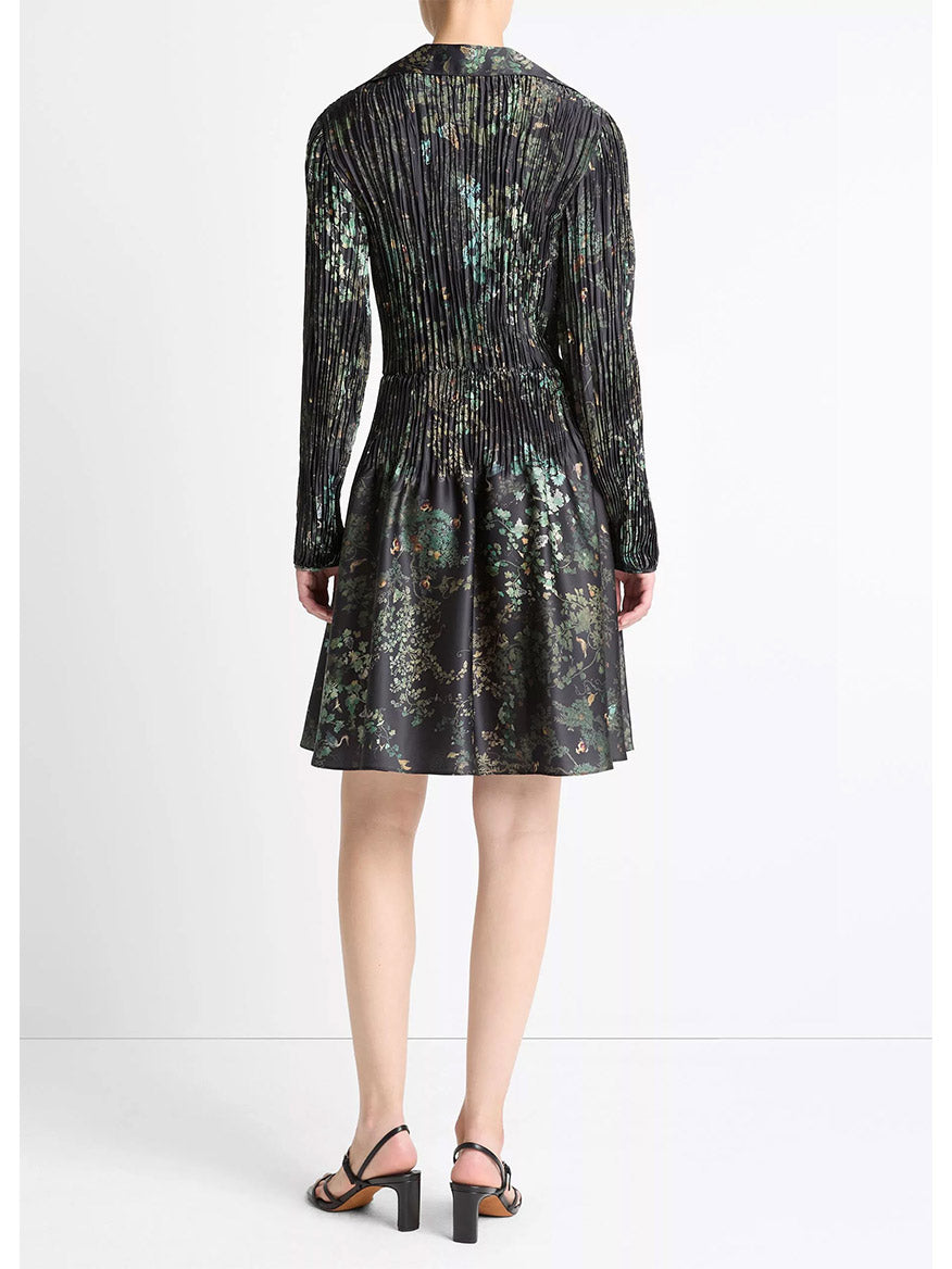 A person faces away, wearing the Vince Grape Vine Crushed Satin Shirt Dress in Black Sky with black heeled sandals against a plain white background.