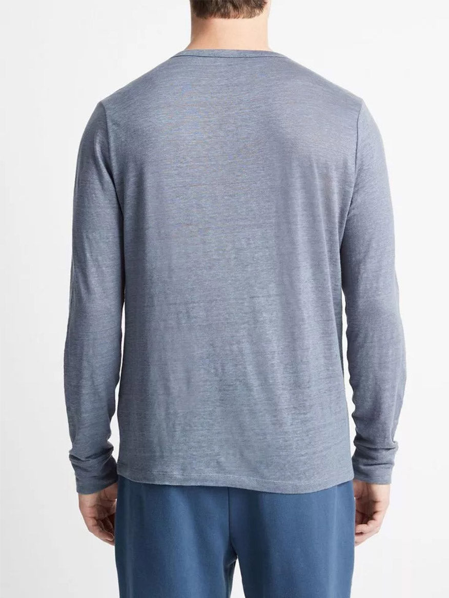 Man standing with his back to the camera, wearing a Vince Linen Long Sleeve Henley in Washed Indigo and blue pants.