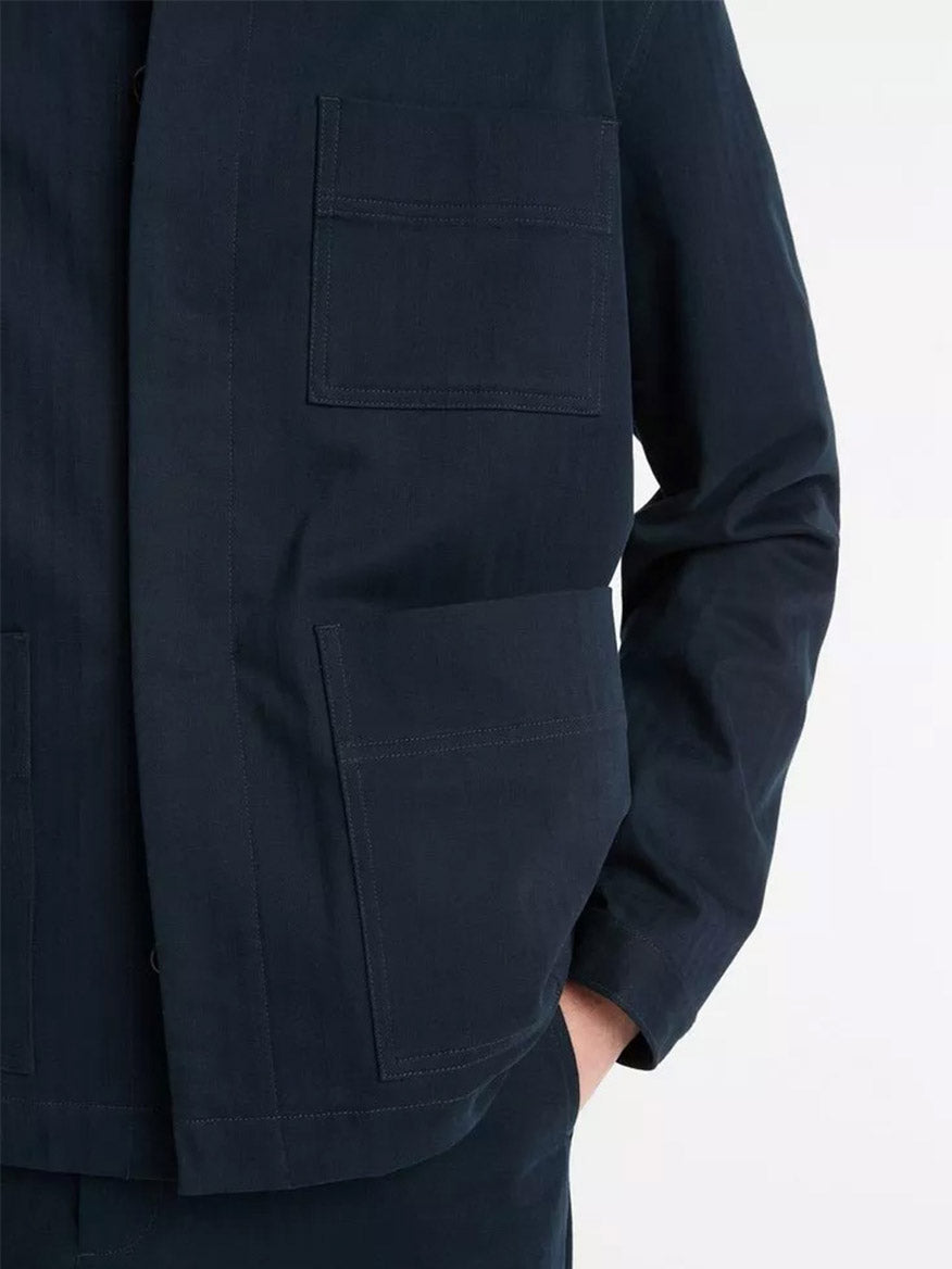 A person wearing a Vince Herringbone Cotton Chore Jacket in Coastal, featuring large front pockets and a subtle plaid lining, casually rests one hand in their pants pocket.