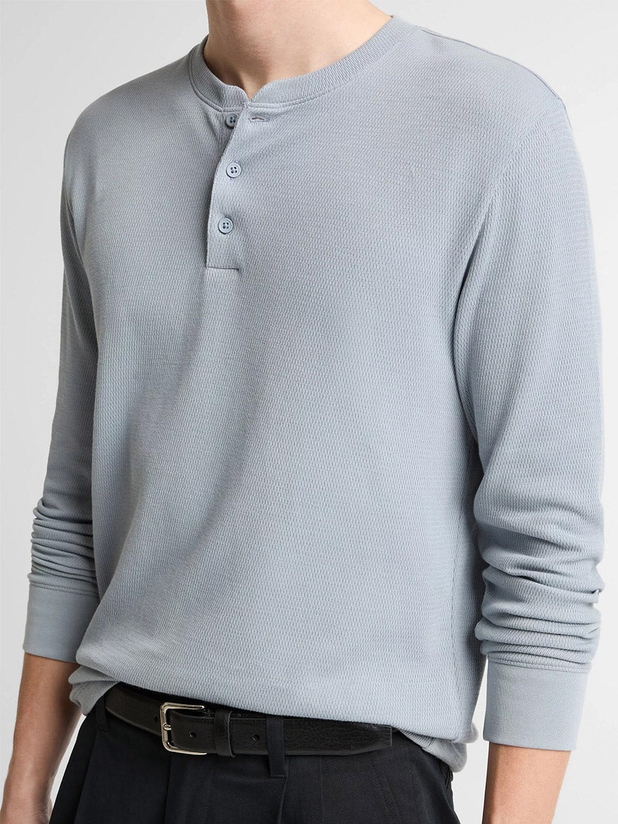 A person wearing a Vince Jacquard-Rib Cotton Henley in Steel Blue with two buttons undone, black pants, and a black belt.