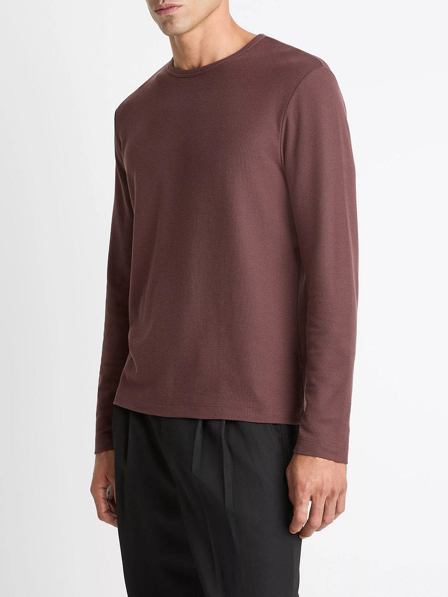 A man wears the Vince Pima Cotton Piqué Long-Sleeve T-Shirt in Washed Port with black pants, standing against a plain white background.