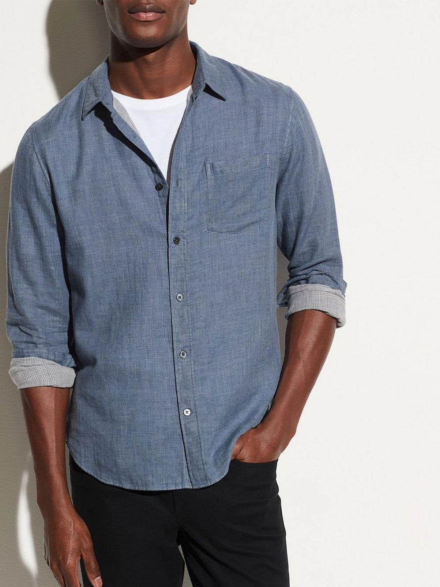 A person stands against a white background, wearing the Vince Double Face Long Sleeve Sport Shirt in Chambray over a white t-shirt, with sleeves rolled up and hands in their pockets.