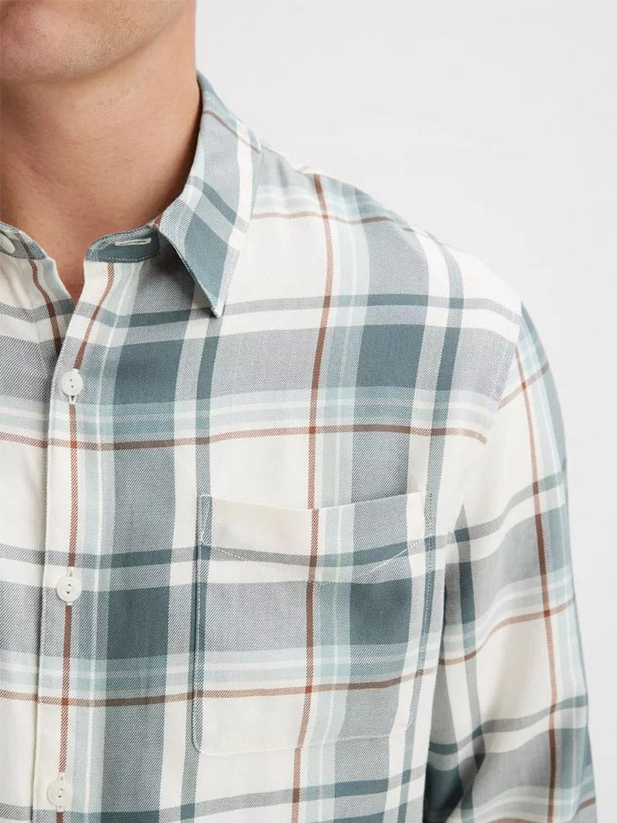 Close-up of a person wearing a Vince Manchester Plaid Shirt in Bone/Dusty Teal. This cotton-blend shirt features a front pocket and button-down collars. The person's face is not visible.