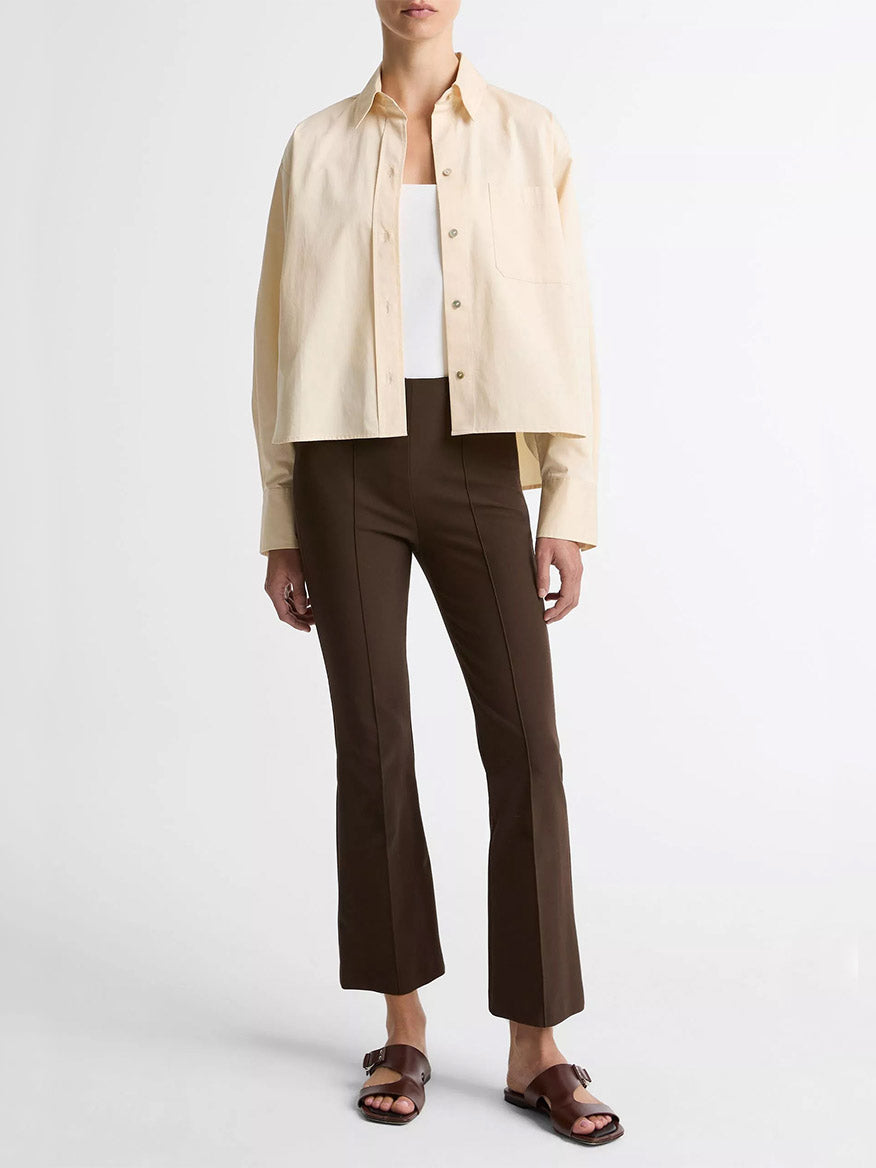 A person in a beige button-up over a white top and Vince Niki Mid-Rise Pintuck Crop Flare Pant in Willow with brown sandals stands against a plain white background.