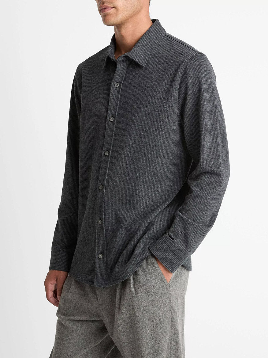 A man wearing the Vince Pinstripe Jacquard Cotton-Blend Button-Front Shirt in Charcoal and light grey pants stands with one hand in his pocket against a plain white background.