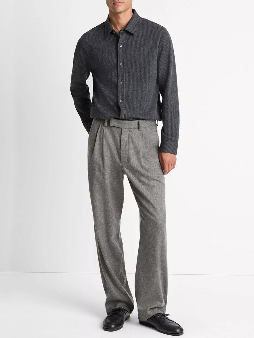 A man stands against a white background wearing a Vince Pinstripe Jacquard Cotton-Blend Button-Front Shirt in Charcoal, light grey pleated pants, and black shoes.