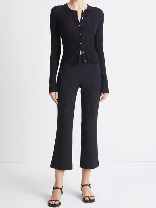 A person wearing a black ribbed button-up sweater and Vince Mid-Rise Pintuck Crop Flare Pant in Coastal Blue paired with strap sandals, standing against a plain background.