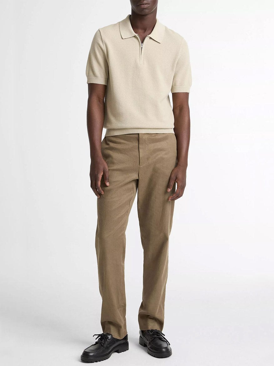 A person stands against a plain background wearing the Vince Cotton-Cashmere Piqué Zip Polo Sweater in Parchment, light brown trousers, and black shoes.