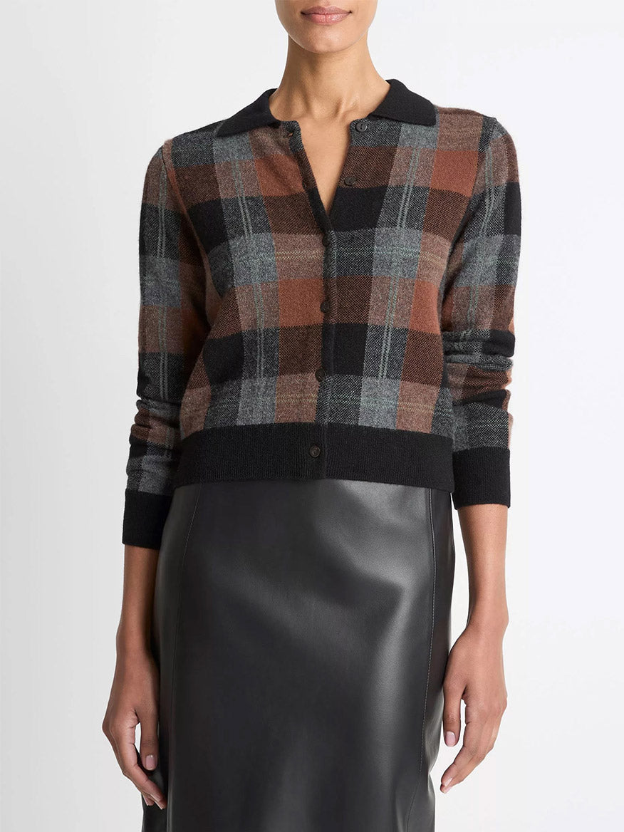 A person wears the Vince Checked Plaid Cashmere Polo Cardigan in Cacao/Dark Heather Pewter/Black with a black faux leather skirt.