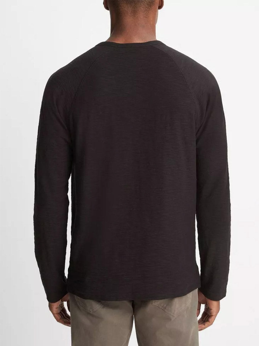 A person wearing the Vince Cotton Long Sleeve Pocket Crew T-Shirt in black, crafted from soft Peruvian cotton, and gray pants is shown from the back against a plain background.